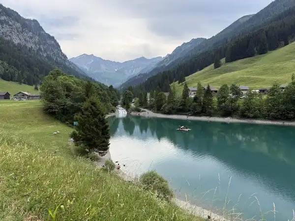 An alpine valley with a turquoise lake, green meadows and steep forested slopes