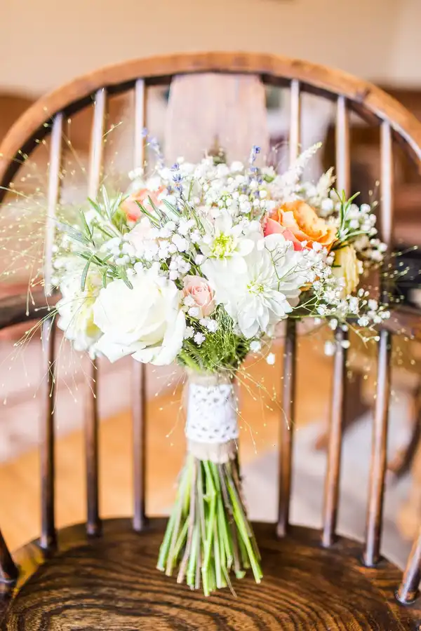 A bouquet of white and peach wedding flowers resting on a wooden chair