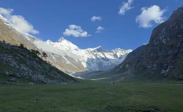 Snow-capped mountains above a wide green valley under a blue sky with scattered clouds